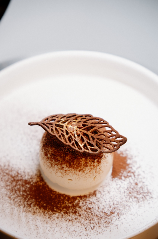 Dessert with a leaf-shaped chocolate decoration on a white plate