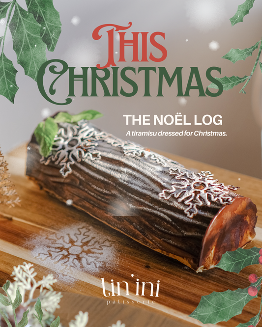 Christmas-themed log cake dessert with decorative elements on a wooden board, featuring the brand 'tin'ini'.