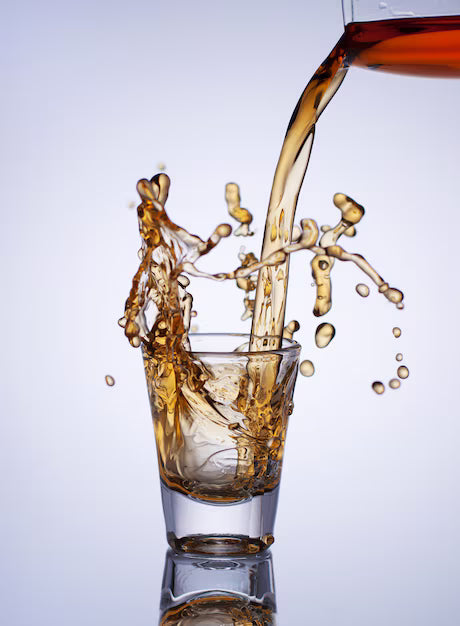 Alcohol being poured into a glass with a splash on a light gray background